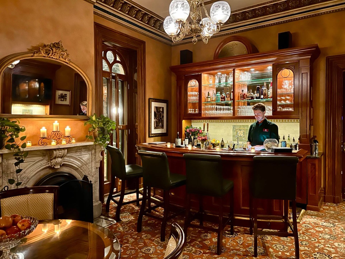 A bartender at the Mansion Hill Inn's mahogany bar, beside a carved marble fireplace and candlelight