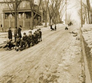 A sepia-toned photo of children sledding down a snow-covered street.